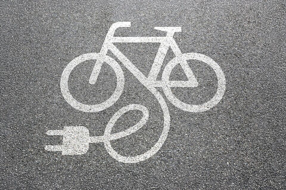 Grafik weißes Fahrrad mit Stecker dran auf Asphalt
